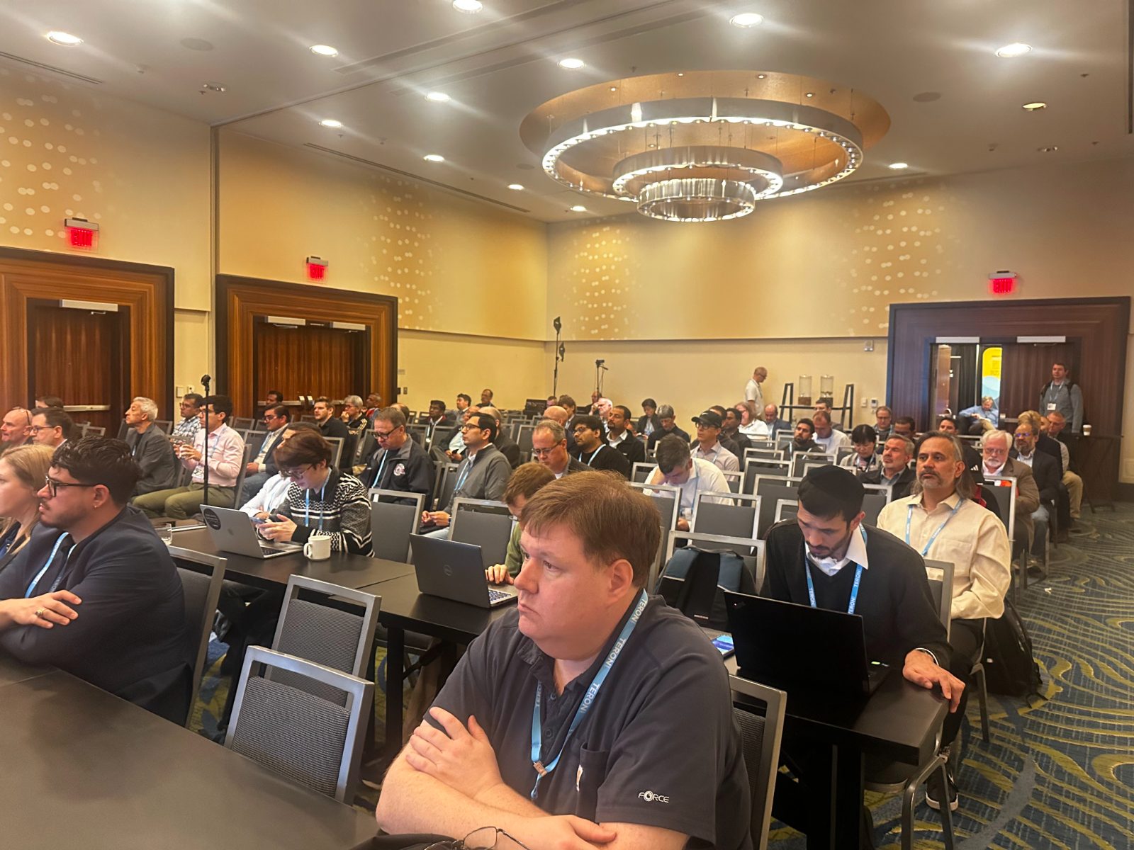 A packed Salon 1 at ICMC26 — rows of attendees listening, many with laptops open, the grand Renaissance-Arlington chandelier above.