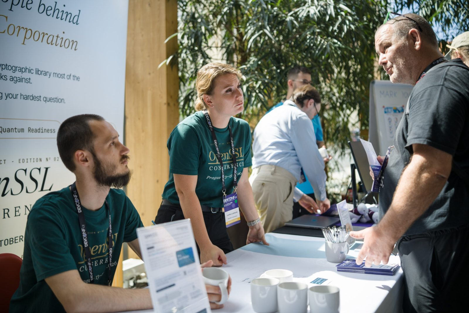 Booth staff talking with an attendee across the booth table, mugs and brochures on the table