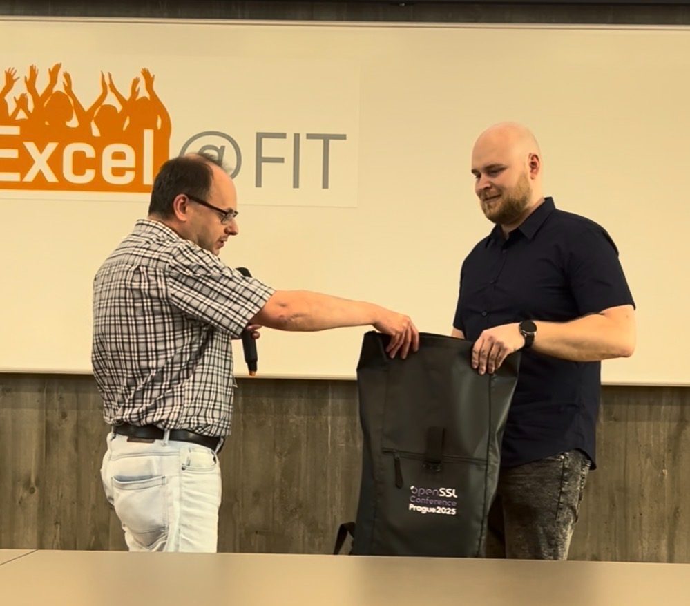Milan Brož handing
                                        the OpenSSL Conference 2025 bag to a prize winner, beneath the Excel@FIT backdrop